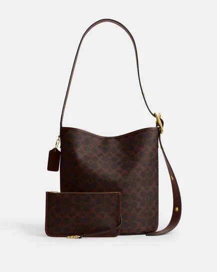 Coach Bleecker Bucket Bag in signature canvas with wine-colored leather trim and adjustable shoulder strap.